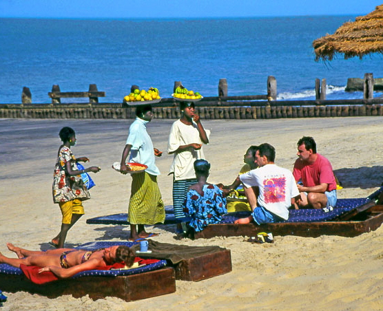 GAMBIA, fruit sellers with tourists, on beach, GAM908JPL A 452 deep